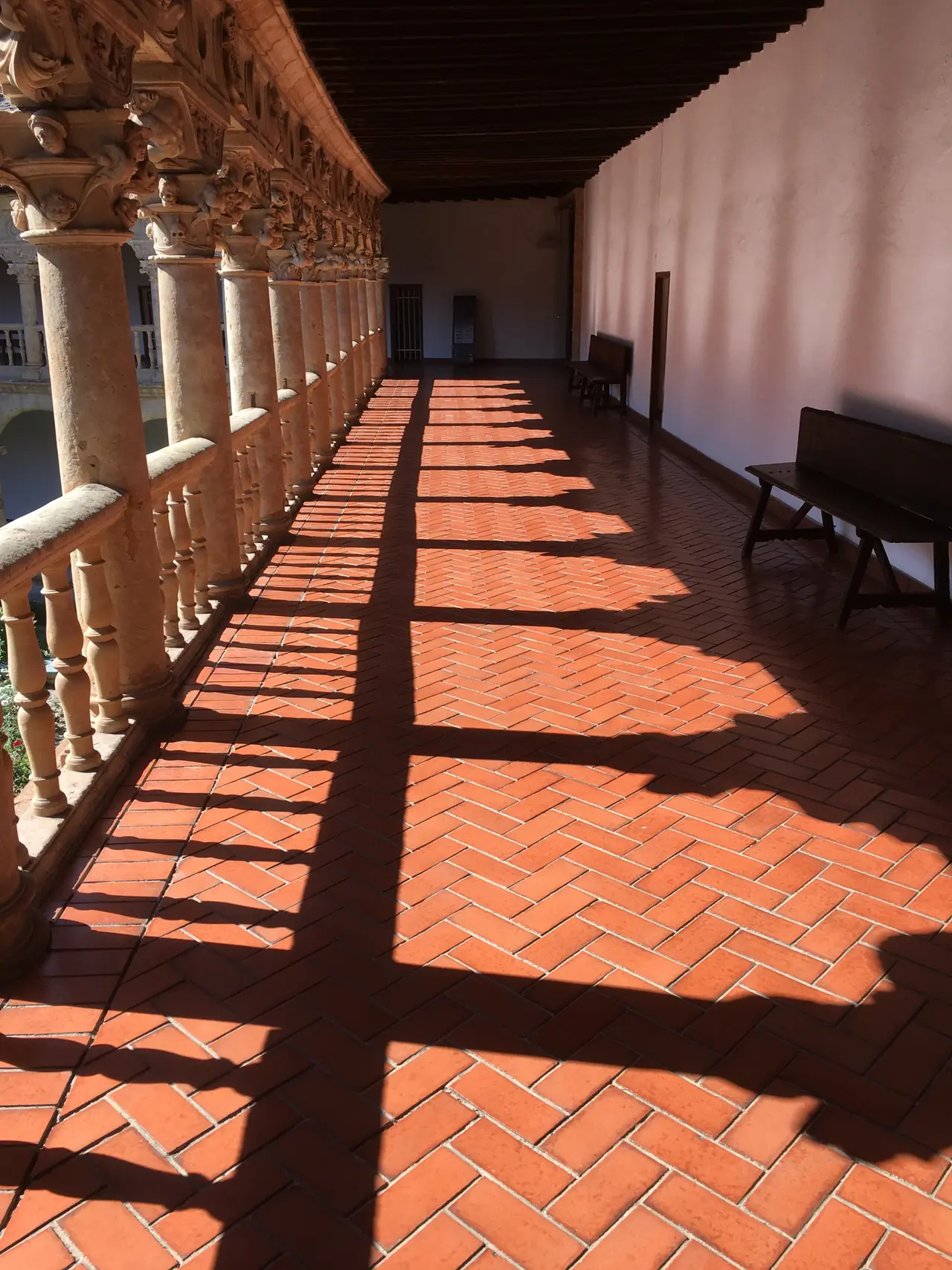 La galería alta del claustro, con la luz entrando entre las columnas sobre el suelo de barro